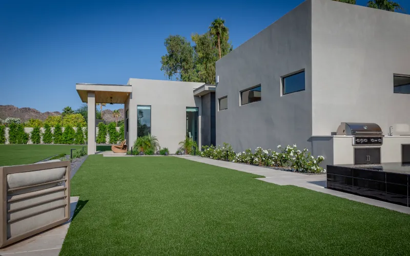 Backyard artificial turf installation with modern home and built-in grill